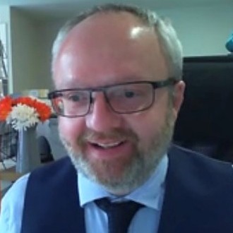 Picture of Ashley Fulwood smiling, wearing blue shirt, dark blue waistcoat and dark blue tie.